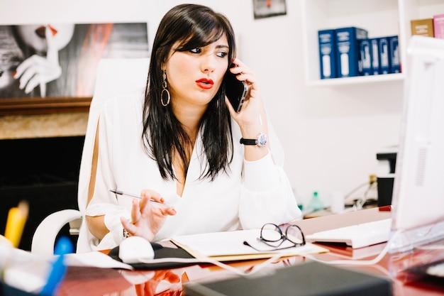 Free photo trendy businesswoman in office talking on phone